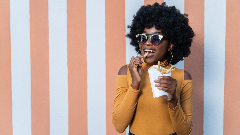 young black woman with afro and sunglasses eating french fries