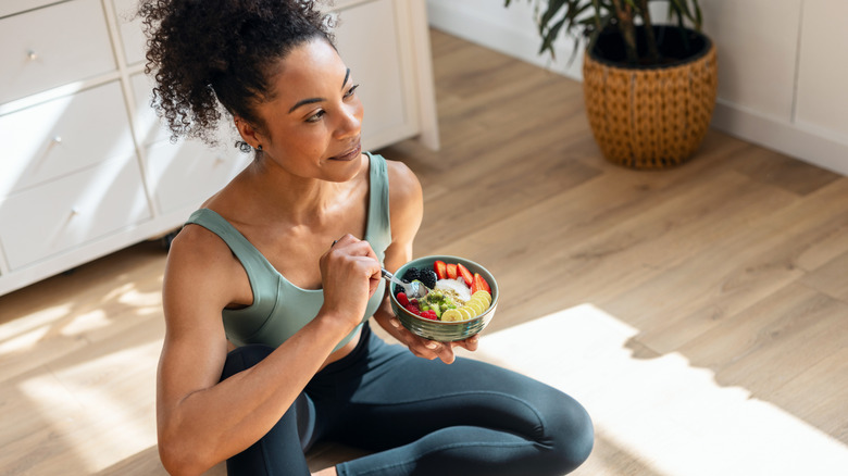 An athletic woman sitting on the floor eating a bowl of fruit