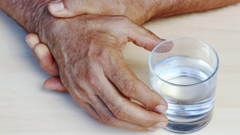 Person with Parkinson's disease reaching glass 