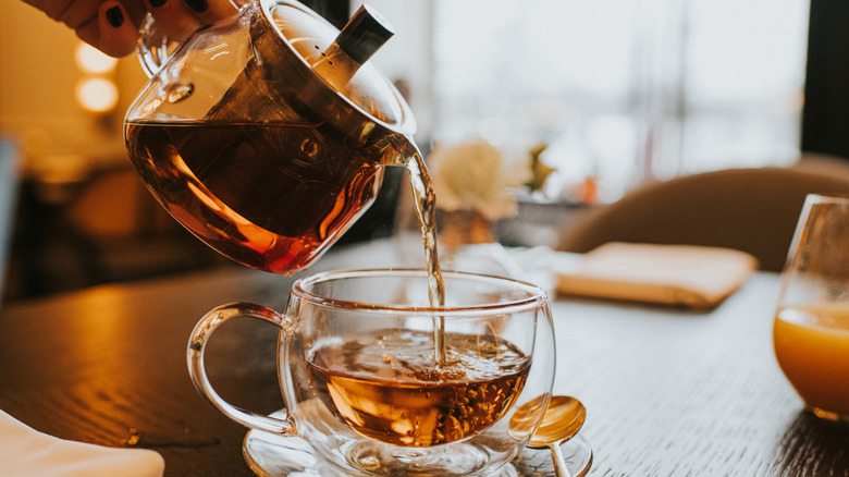 A glass teapot pouring tea into a glass teacup