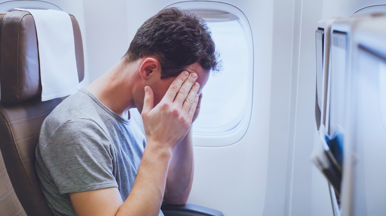 Man on airplane holding his head not feeling well