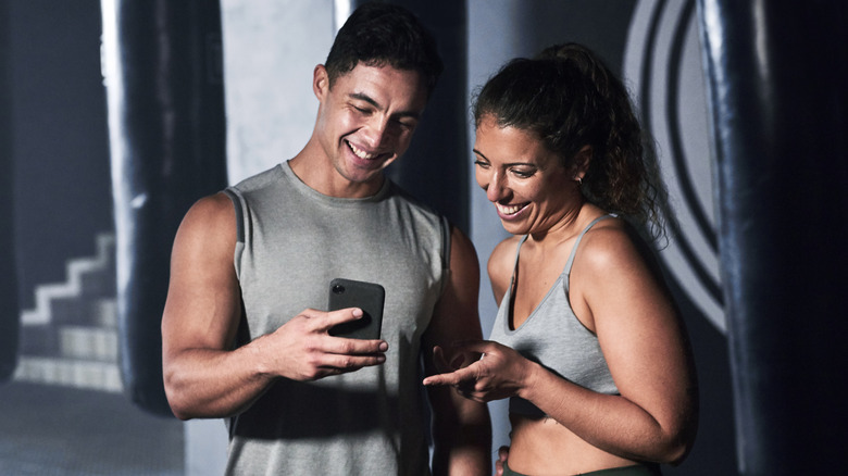 Two people looking at phones in workout clothes at the gym.