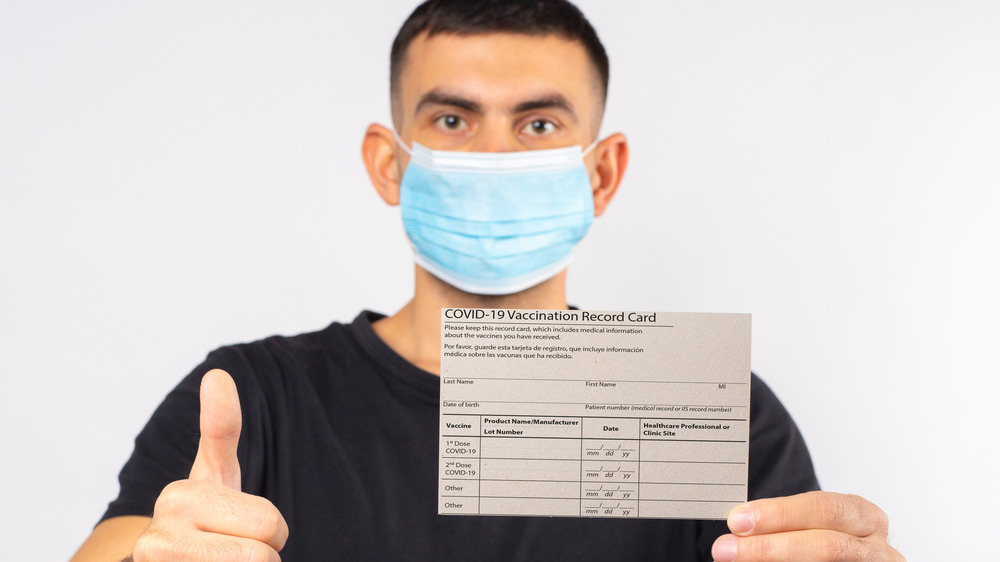 young man wearing face mask holding vaccination card