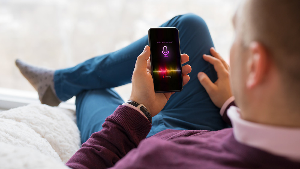 Person wearing purple top and blue pants sitting cross-legged on chair holding cell phone