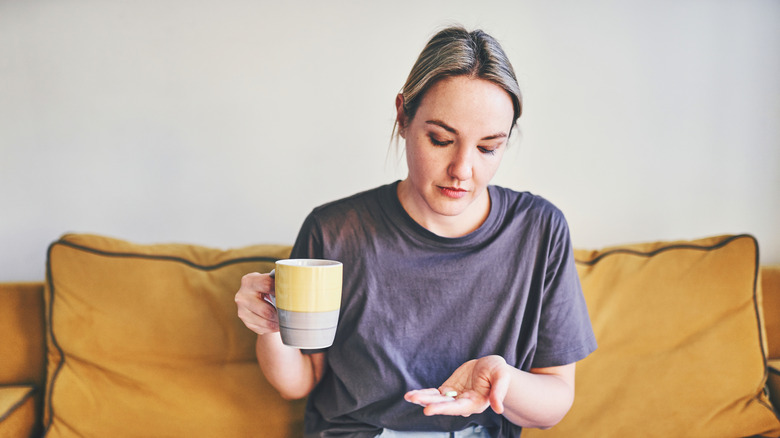 woman holding pill in one hand and mug in other