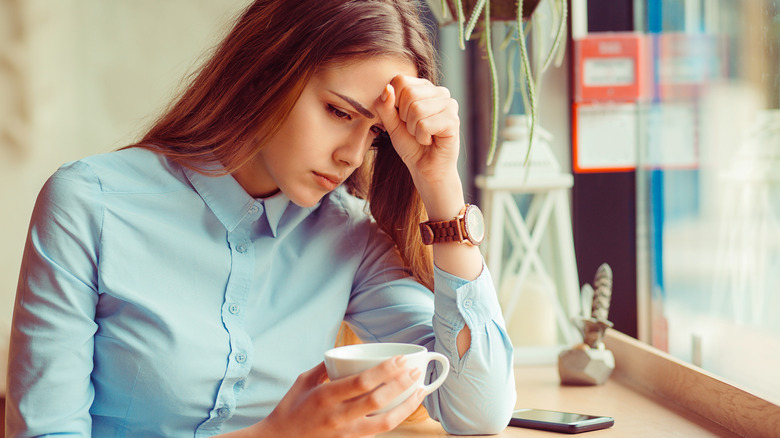 A woman has a headache and drinks a cup of coffee