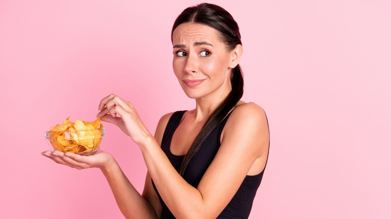 woman with anxious expression eating potato chips