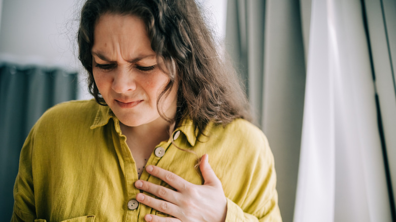A woman wincing while holding her left chest