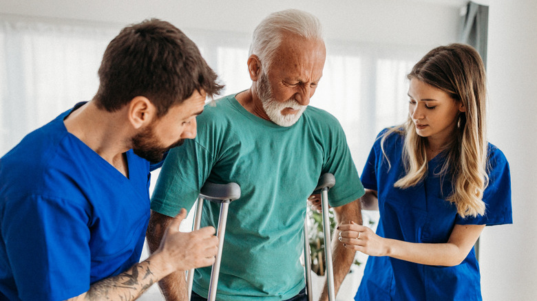 Older man being assisted on crutches