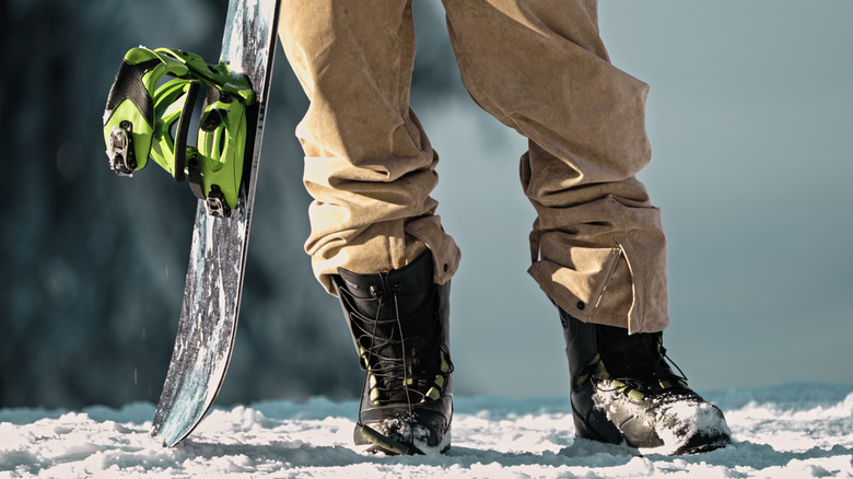 Close up of person's legs standing in the snow next to a snowboard