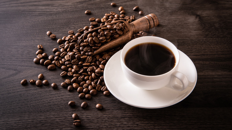A white cup of coffee surrounded by coffee beans
