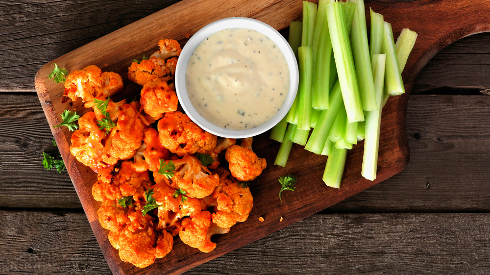 Buffalo cauliflower poppers on a wooden cutting board with celery 