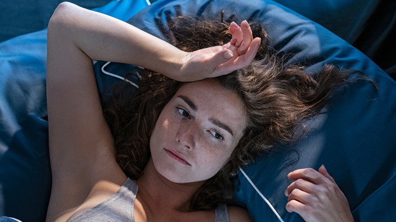 lady awake in bed with blue sheets hand on head