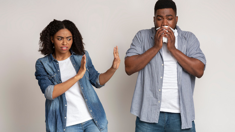 man blowing nose near woman