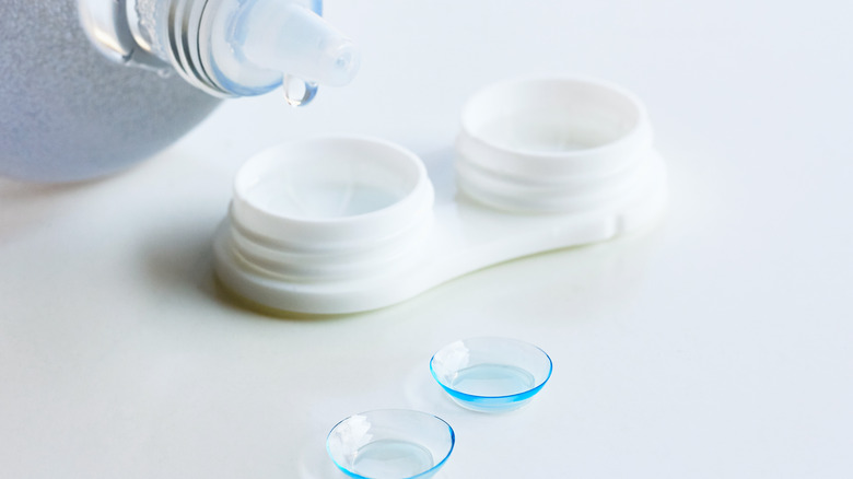 Close up of contact solution being poured into case with two contact lenses on table