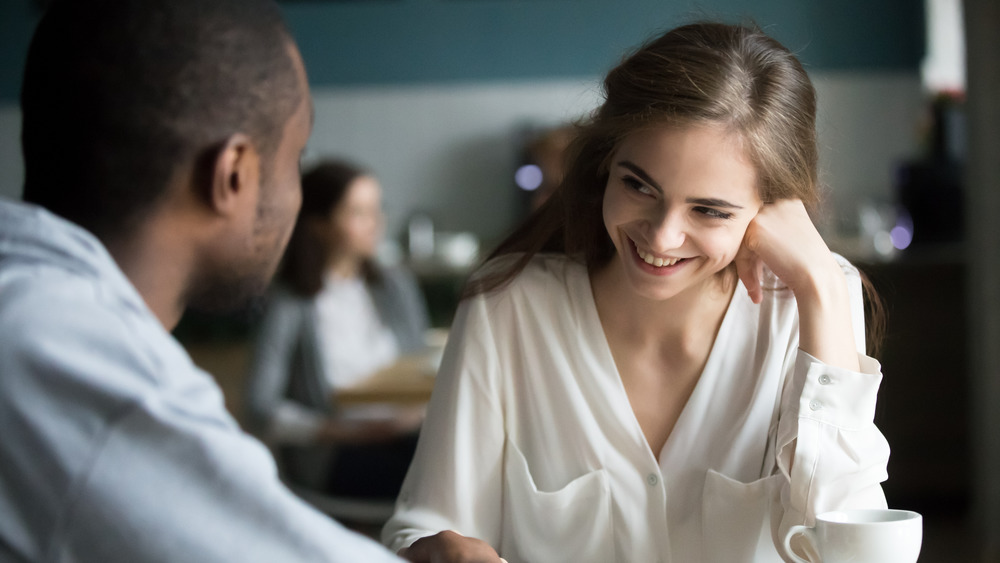 Woman smiling coyly at a man while sitting with coffee 