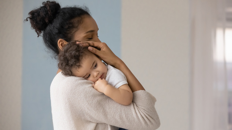 Woman stands holding her baby while breastfeeding and smiling