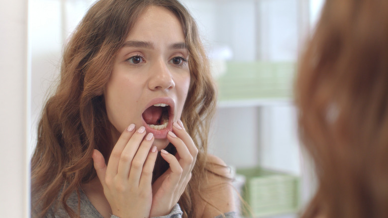 Woman with hands on open jaw examining teeth in mirror