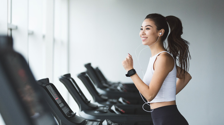 Young woman exercising on treadmill and listening to music in the gym
