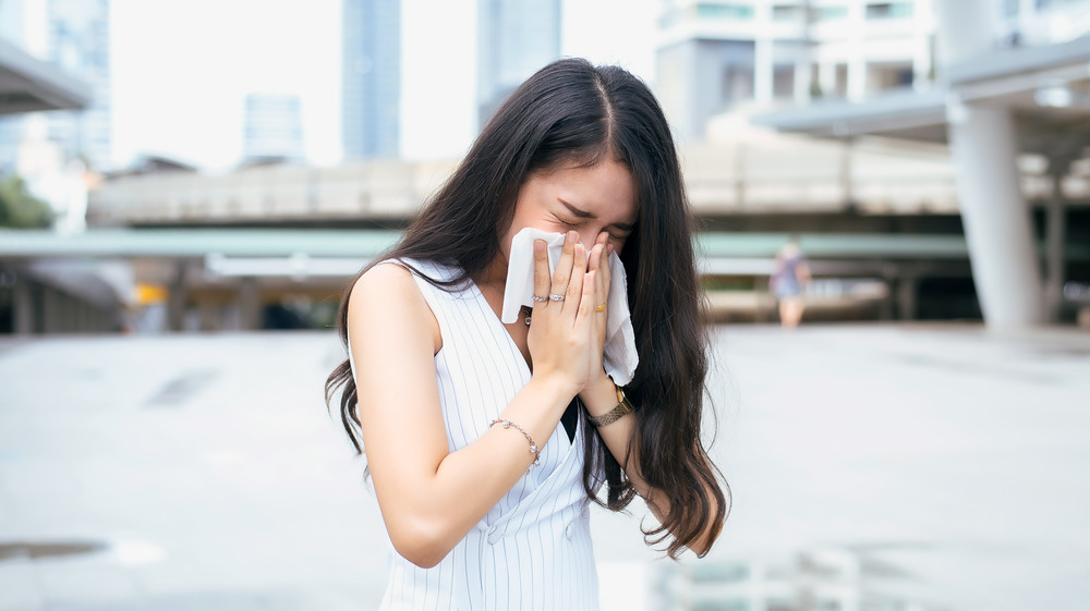 Young woman sneezing into a tissue outside 