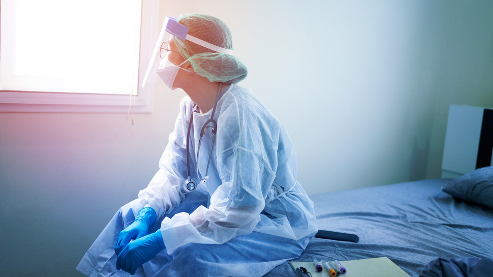 A tired female doctor in full protection looking out the window 