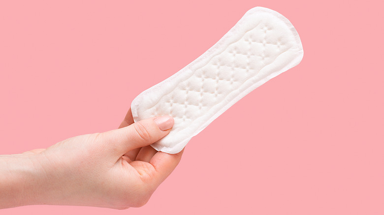 Close up of hand holding a panty liner on pink background