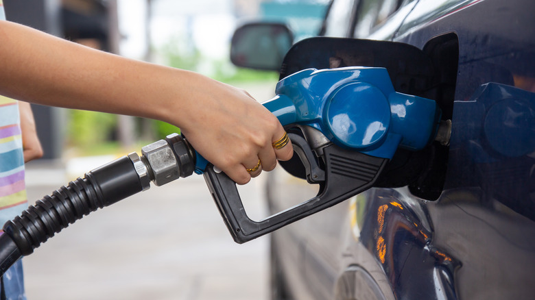 Hand holding a blue gas pump as it pumps gas into car