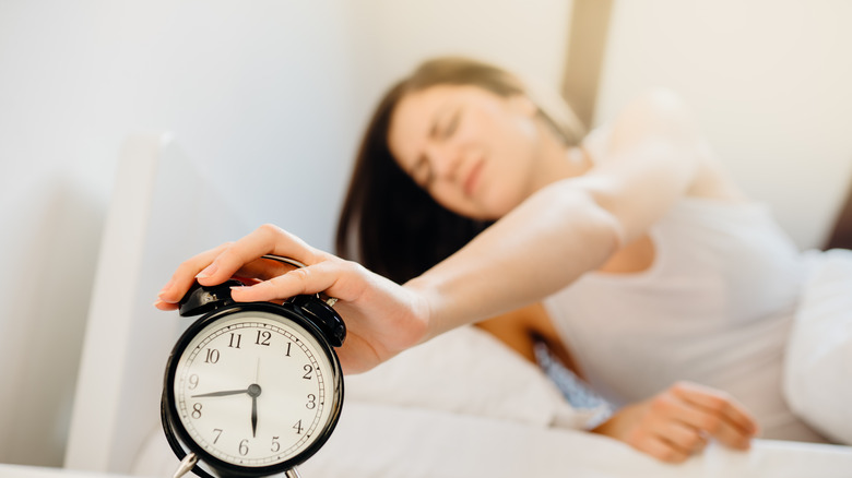 Woman reaching out to turn off alarm clock