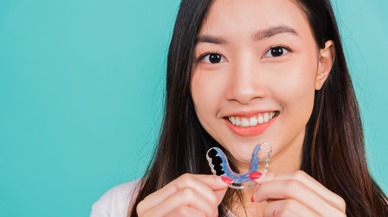 Young woman holding up a blue dental retainer in front of an aqua background