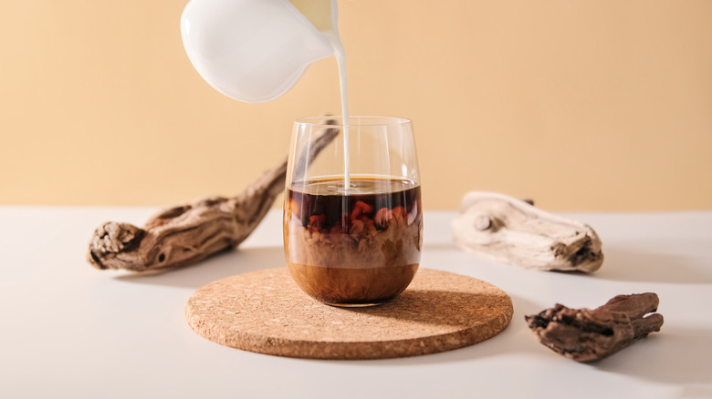Someone pours milk into a cup of coffee