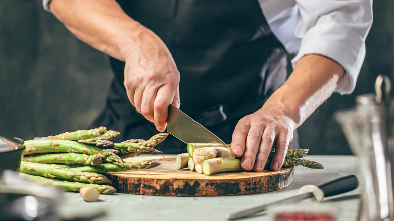 A man chops asparagus on a wooden slab