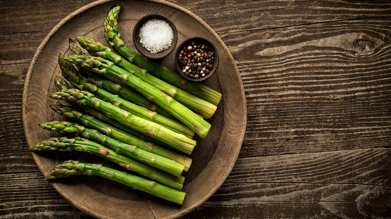 A plate of asparagus sits on a wooden table