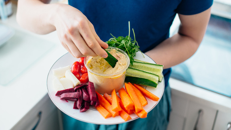 A man is dipping vegetables in hummus