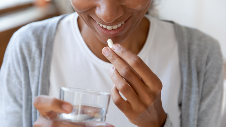 woman taking vitamins with a glass of water 