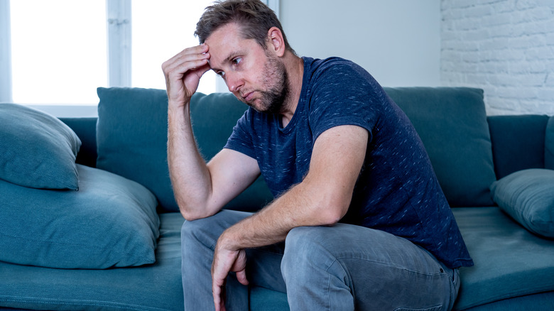 Man sitting on couch hand on head