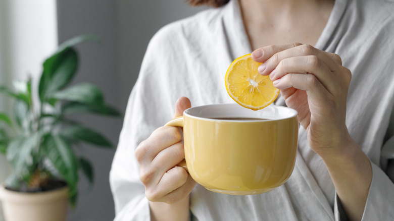 Hand dipping lemon wedge in mug
