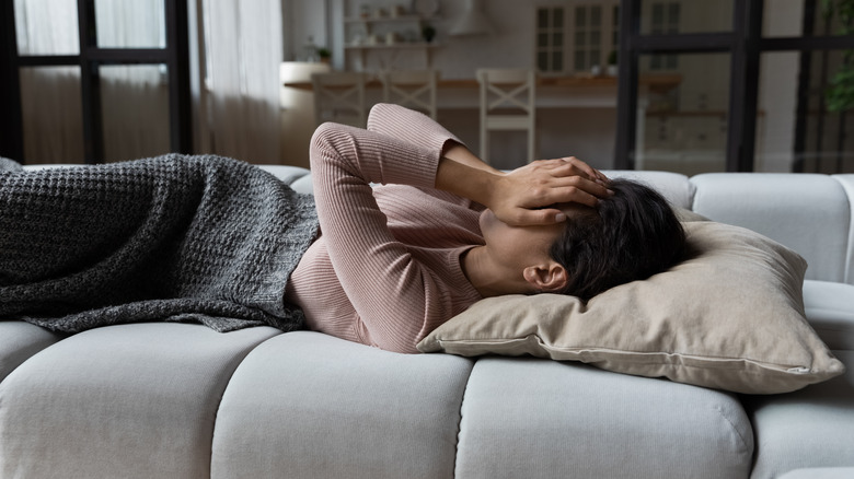 Woman lying on couch with hands over her face