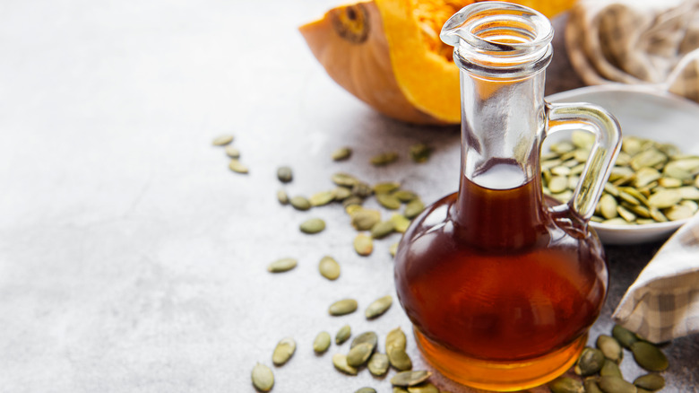 glass jar of pumpkin seed oil with a bowl of pumpkin seeds 