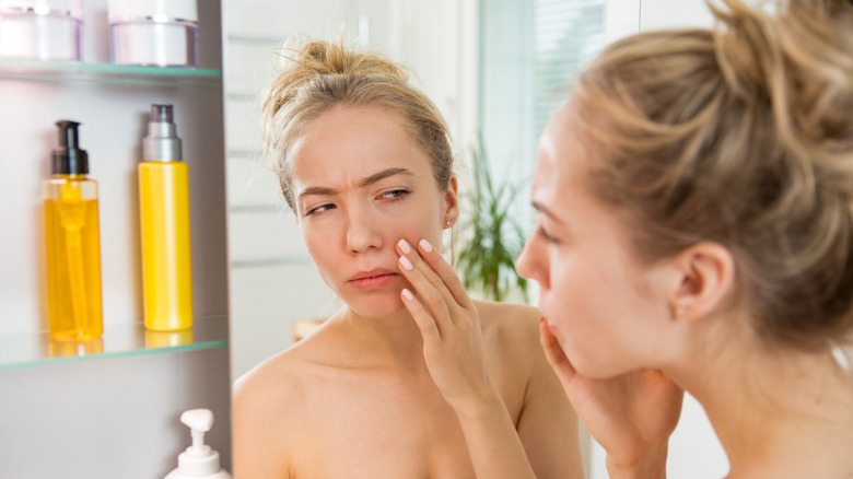 young woman examining her face in the mirror