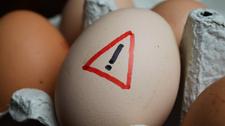 Close up of a raw brown egg with warning sign