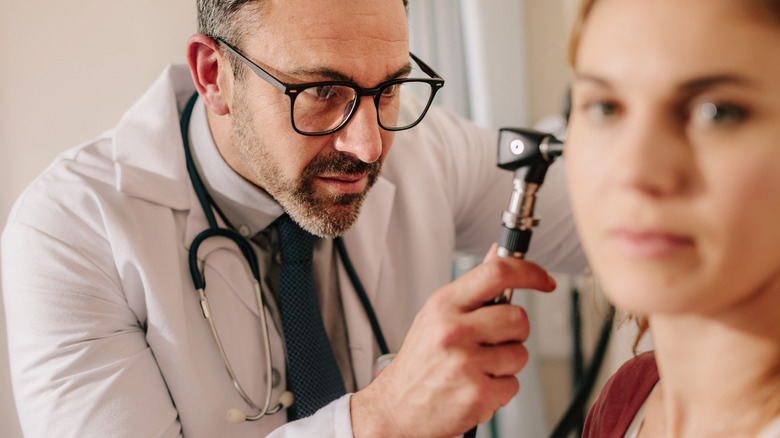 ENT doctor checking ear of woman patient with otoscope 