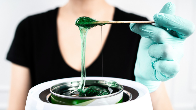 Beauty technician holding up wooden stick with melted wax