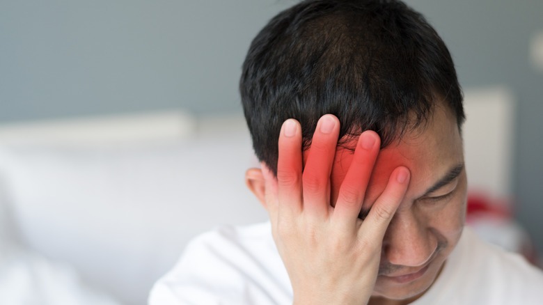 Man pressing on side of his head highlighted in red