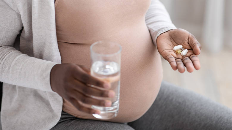 Pregnant woman taking vitamins with glass of water