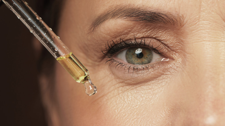 Young woman applying anti-aging serum to her face 