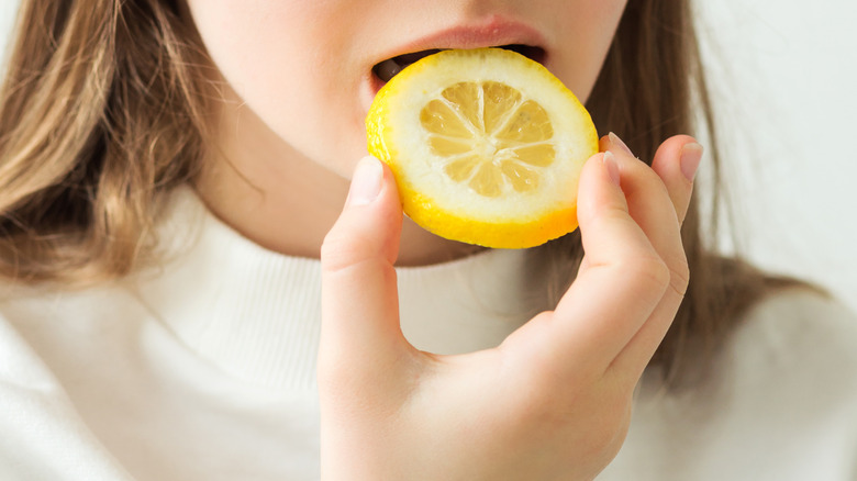 Woman biting down on a slice of lemon