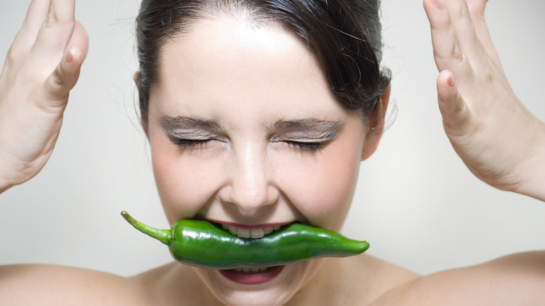 woman holding a spicy green chili in her mouth 