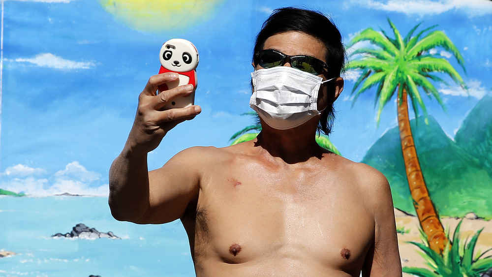 Close shot of a topless man taking a selfie while wearing a face mask