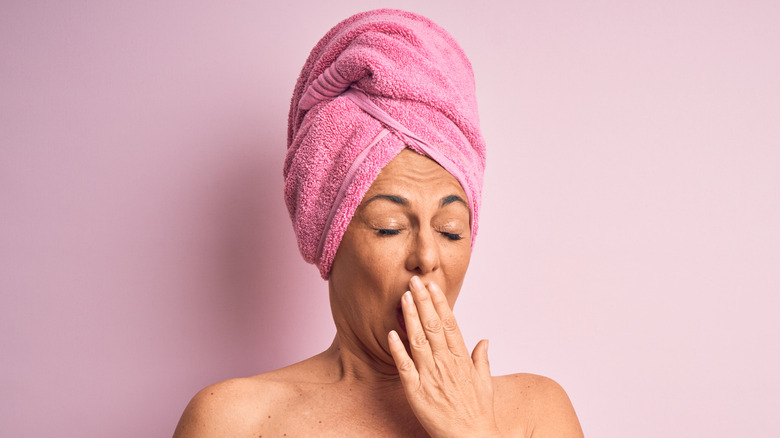 woman in a pink towel yawning with isolated pink background 