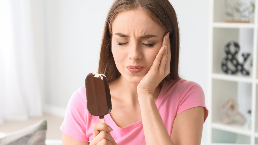 Woman eating an ice cream pop holds her cheek in pain